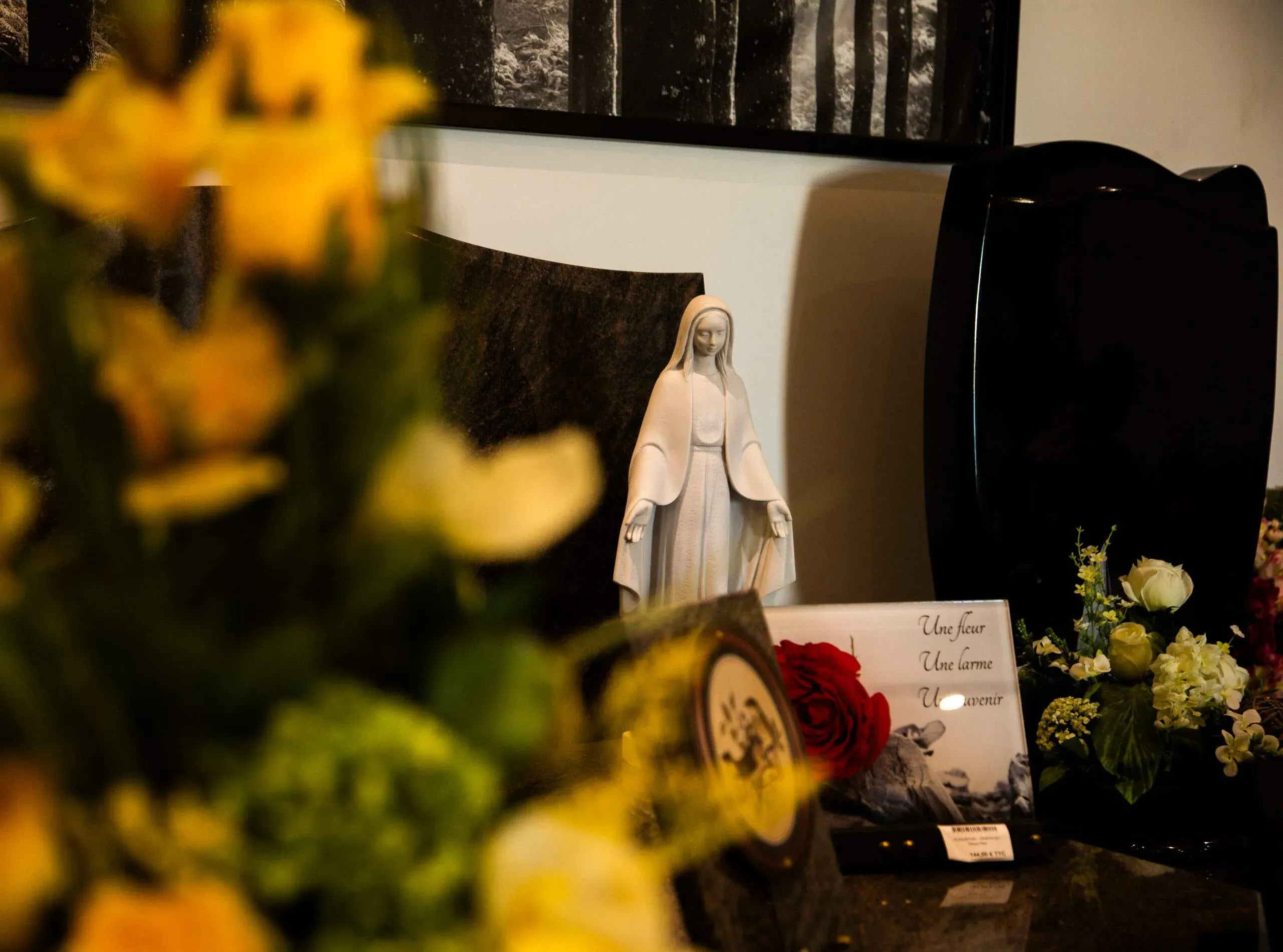 Statuette de la Vierge Marie et plaque funéraire présentées avec des fleurs