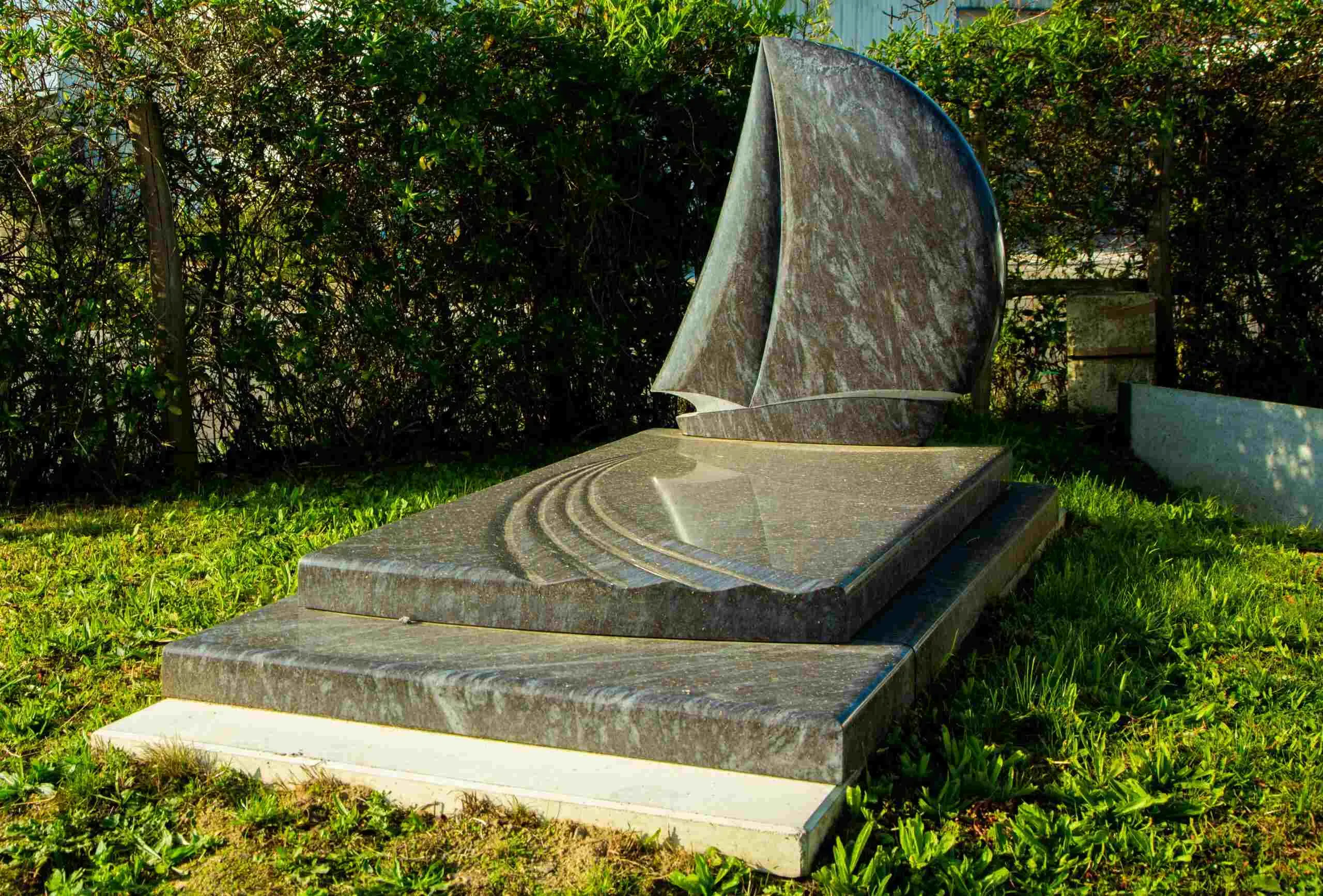 Monument funéraire original en granite sculpté en forme de voilier sur herbe